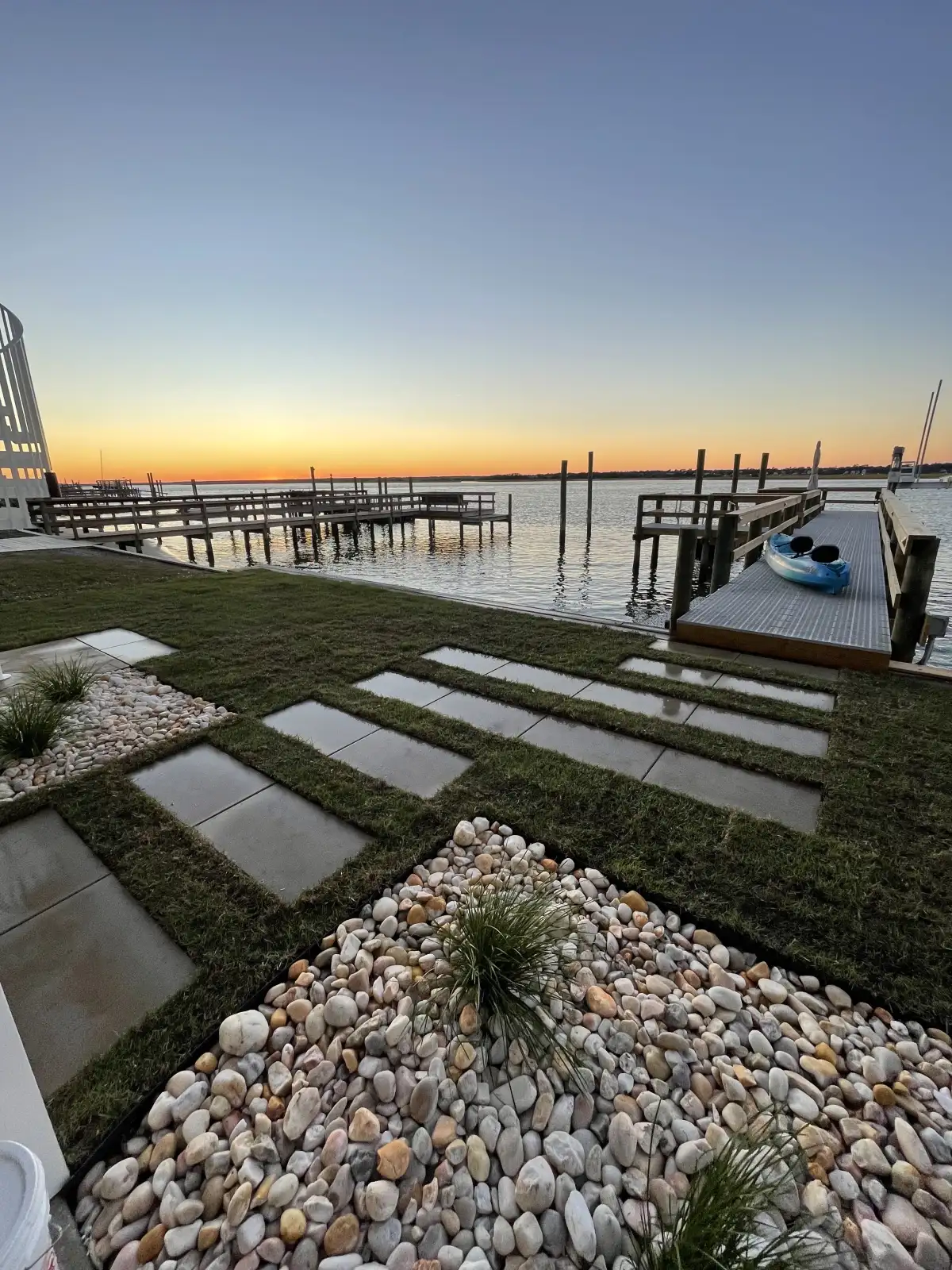Completed waterfront landscape with stepping stones, gravel, lawn, and a sunset view