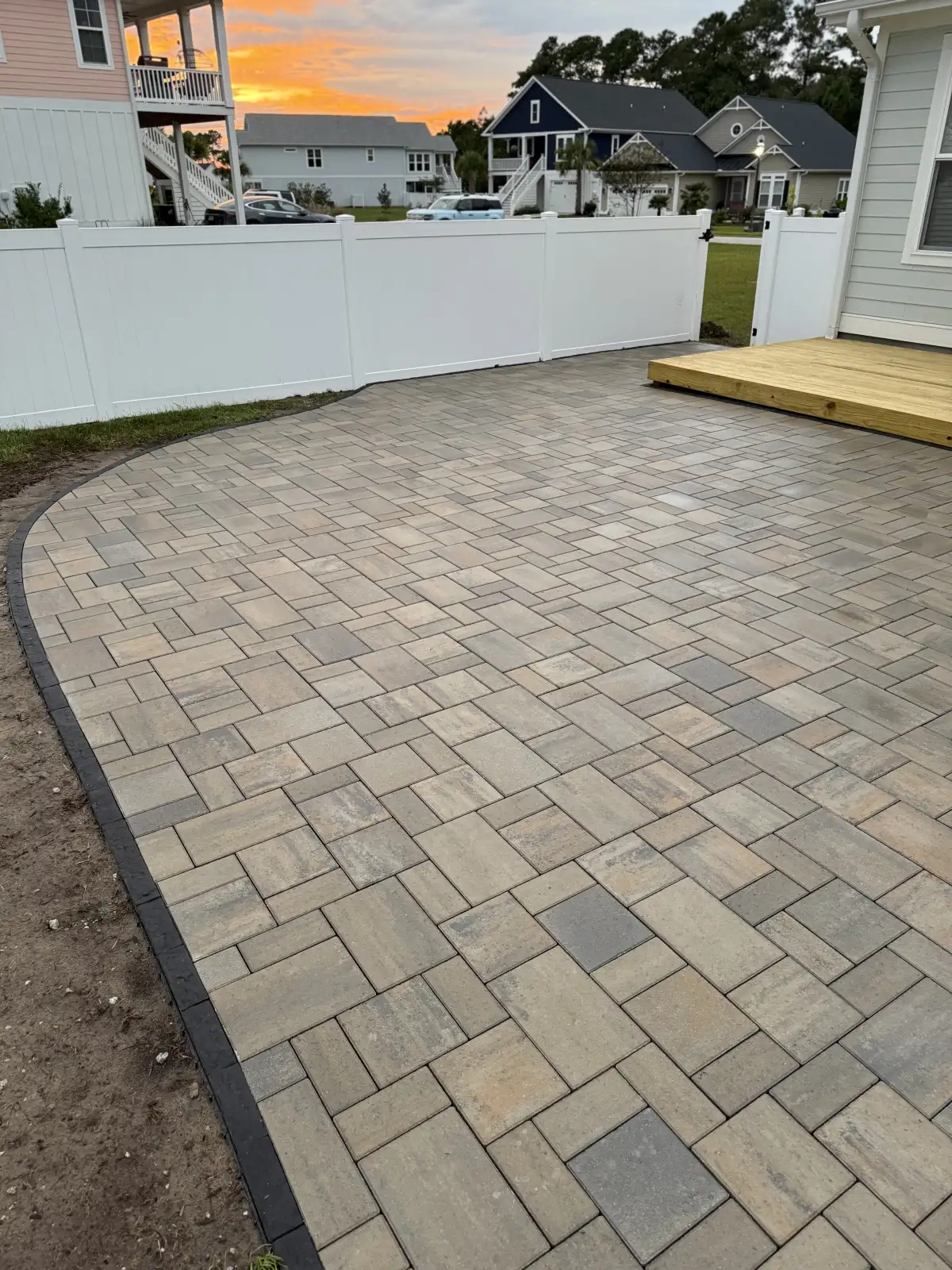Finished curved paver patio with a contrasting border beside a backyard deck