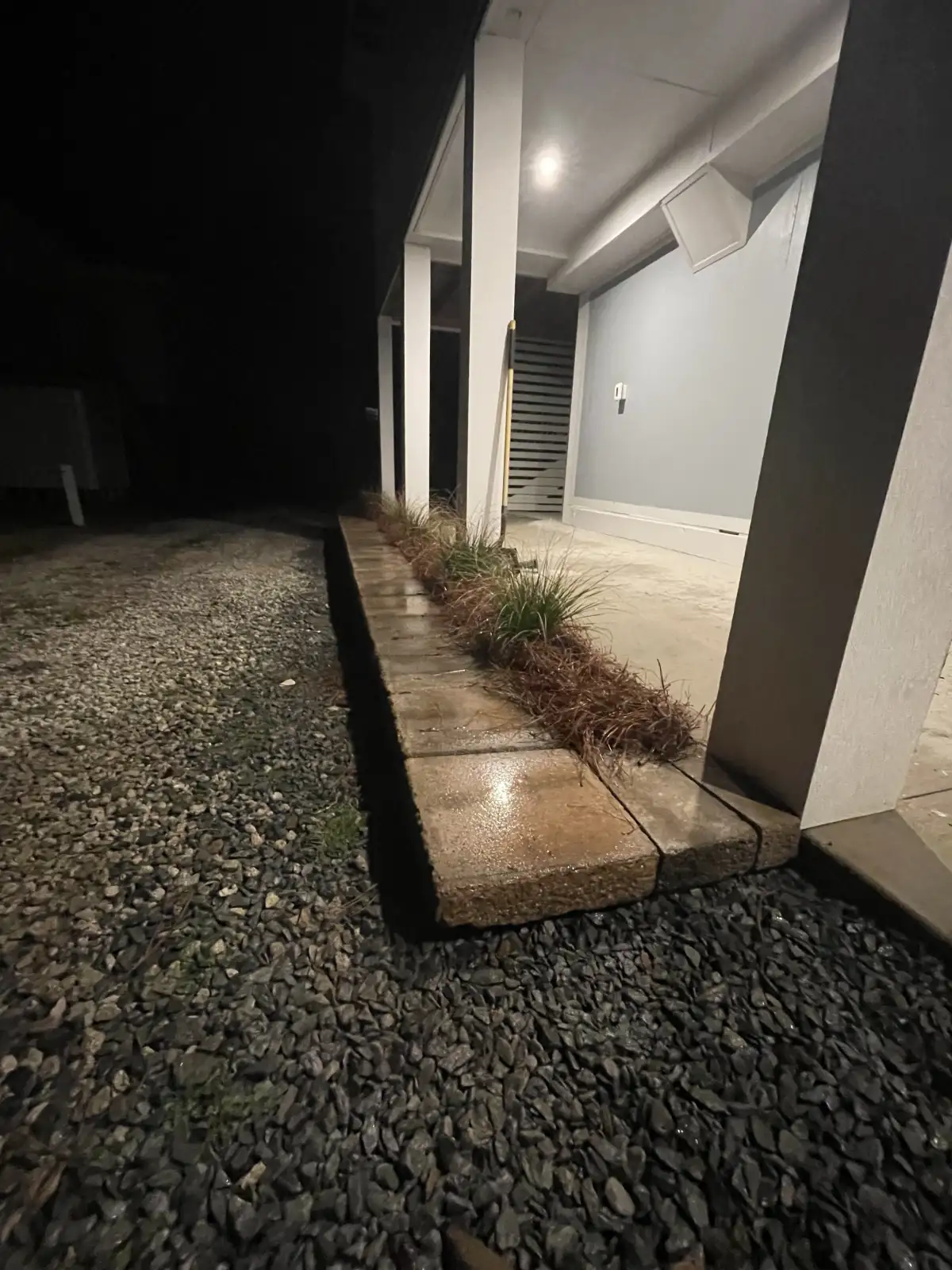 Warm exterior downlighting illuminating a covered walkway and planting bed at night